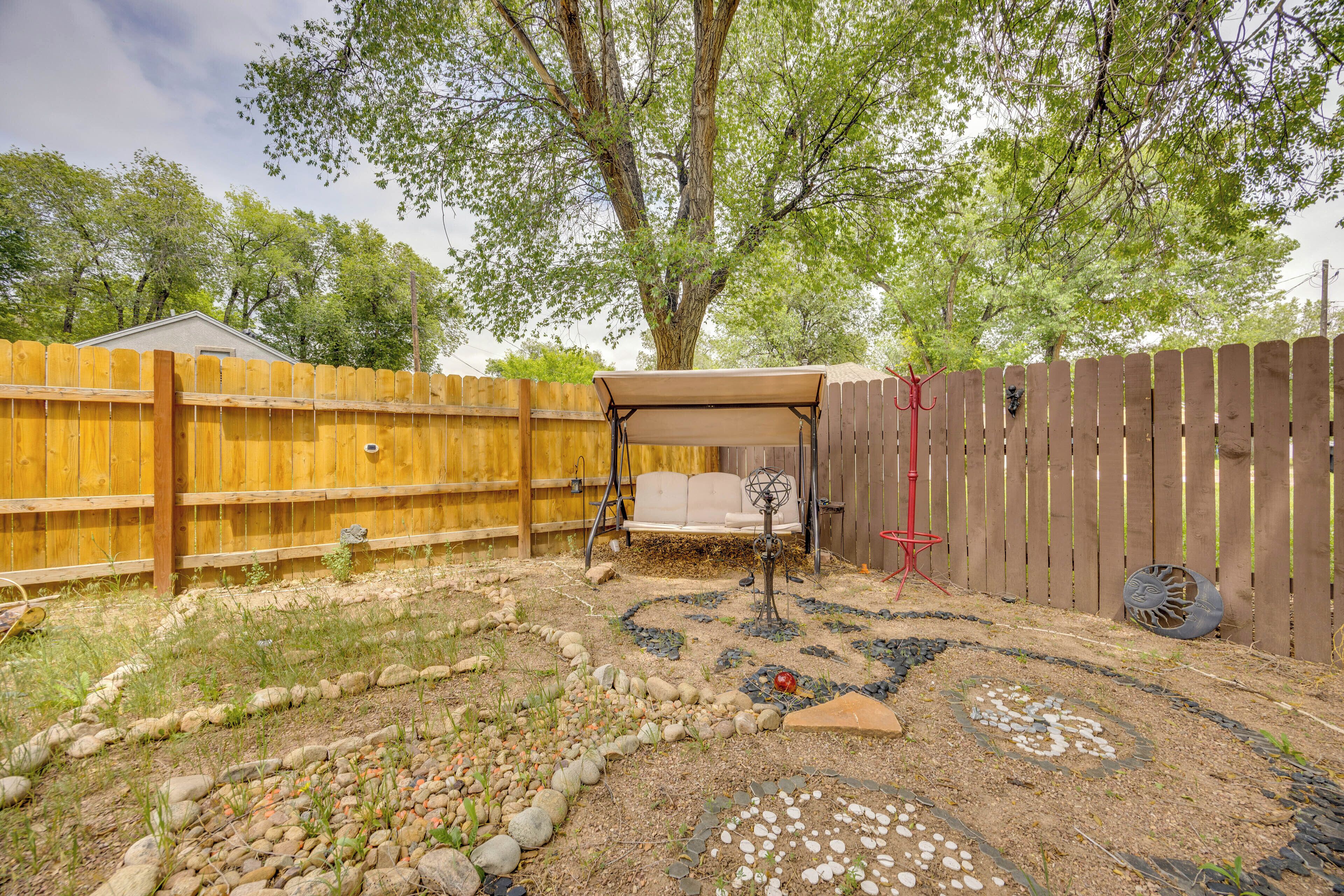 A backyard with a wooden fence, a covered seating area, and a decorative garden.