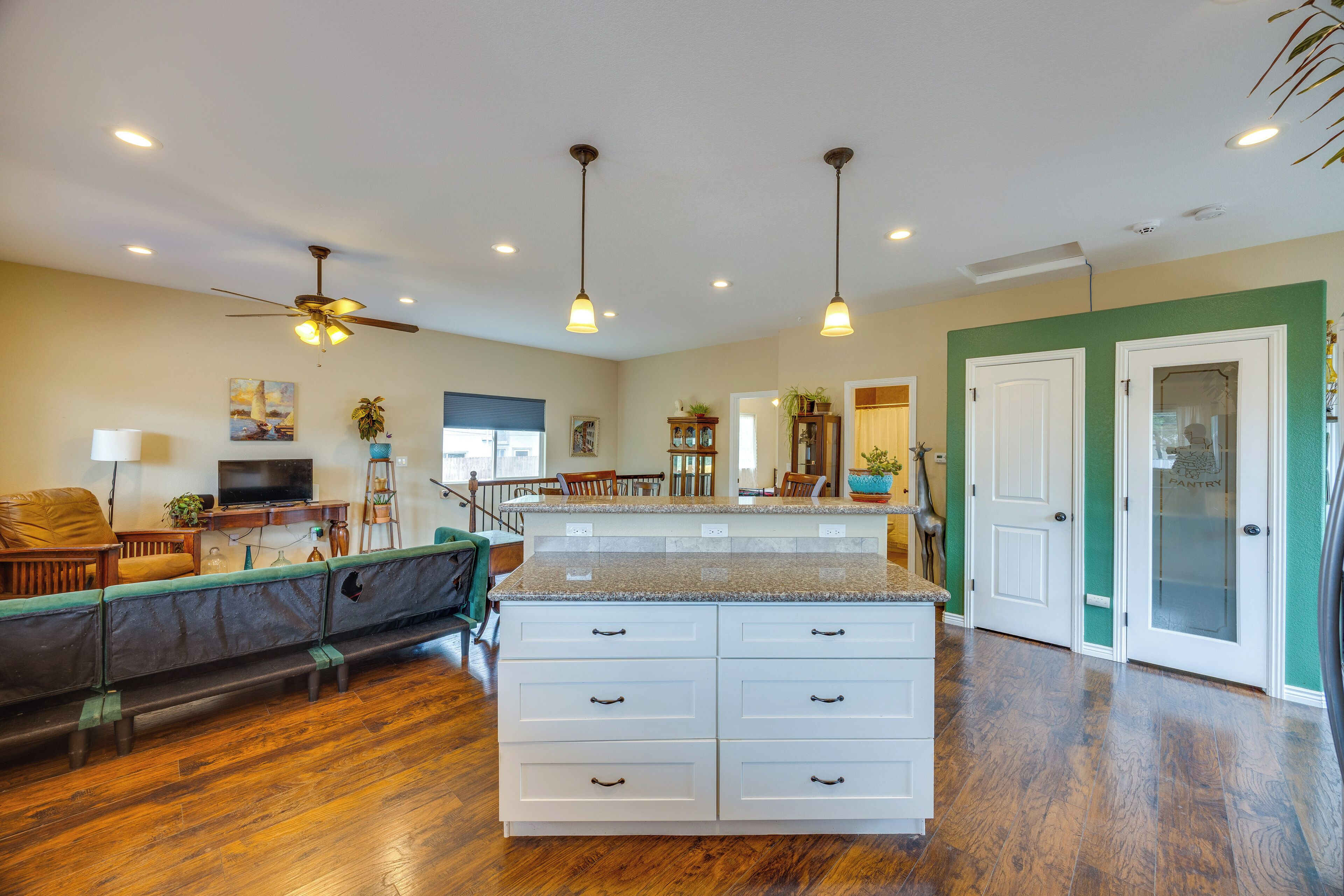 A spacious kitchen with a central island, wooden flooring, pendant lighting, and a view into the dining area.