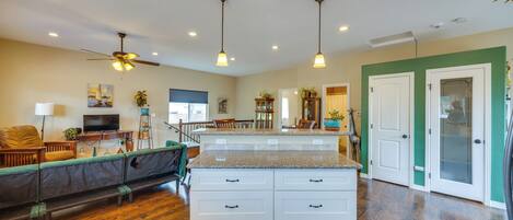 A spacious kitchen with a central island, wooden flooring, pendant lighting, and a view into the dining area.