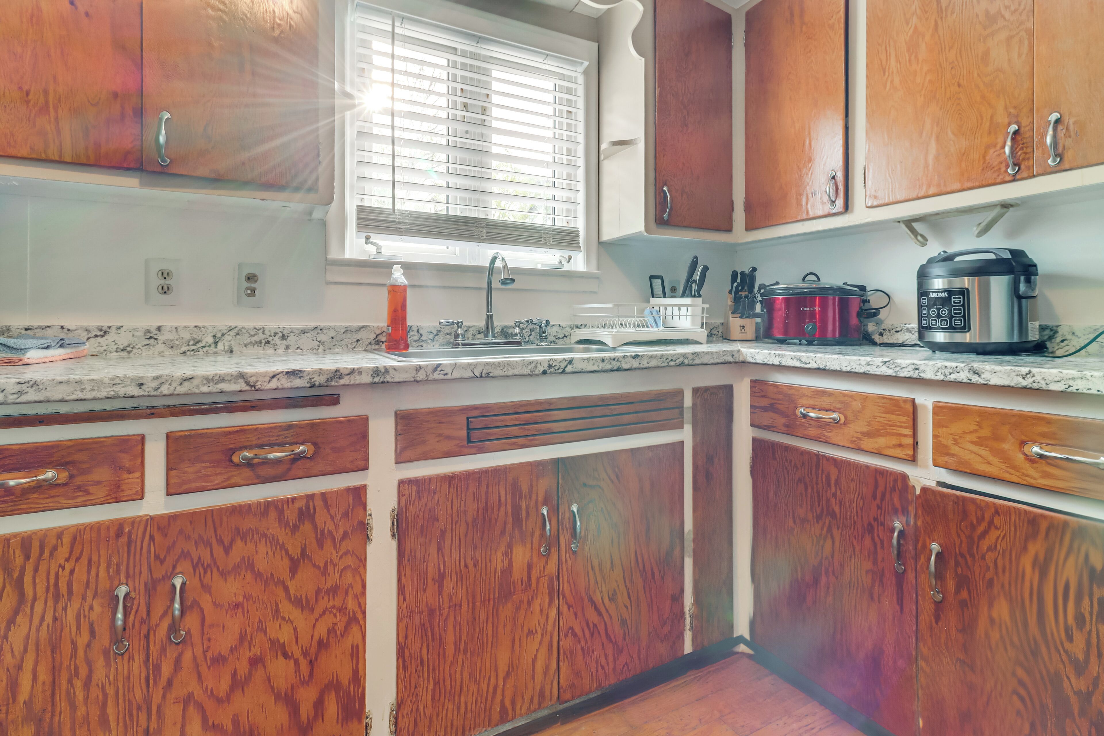 A kitchen with wooden cabinets, a sink, a window with blinds, and a coffee maker.
