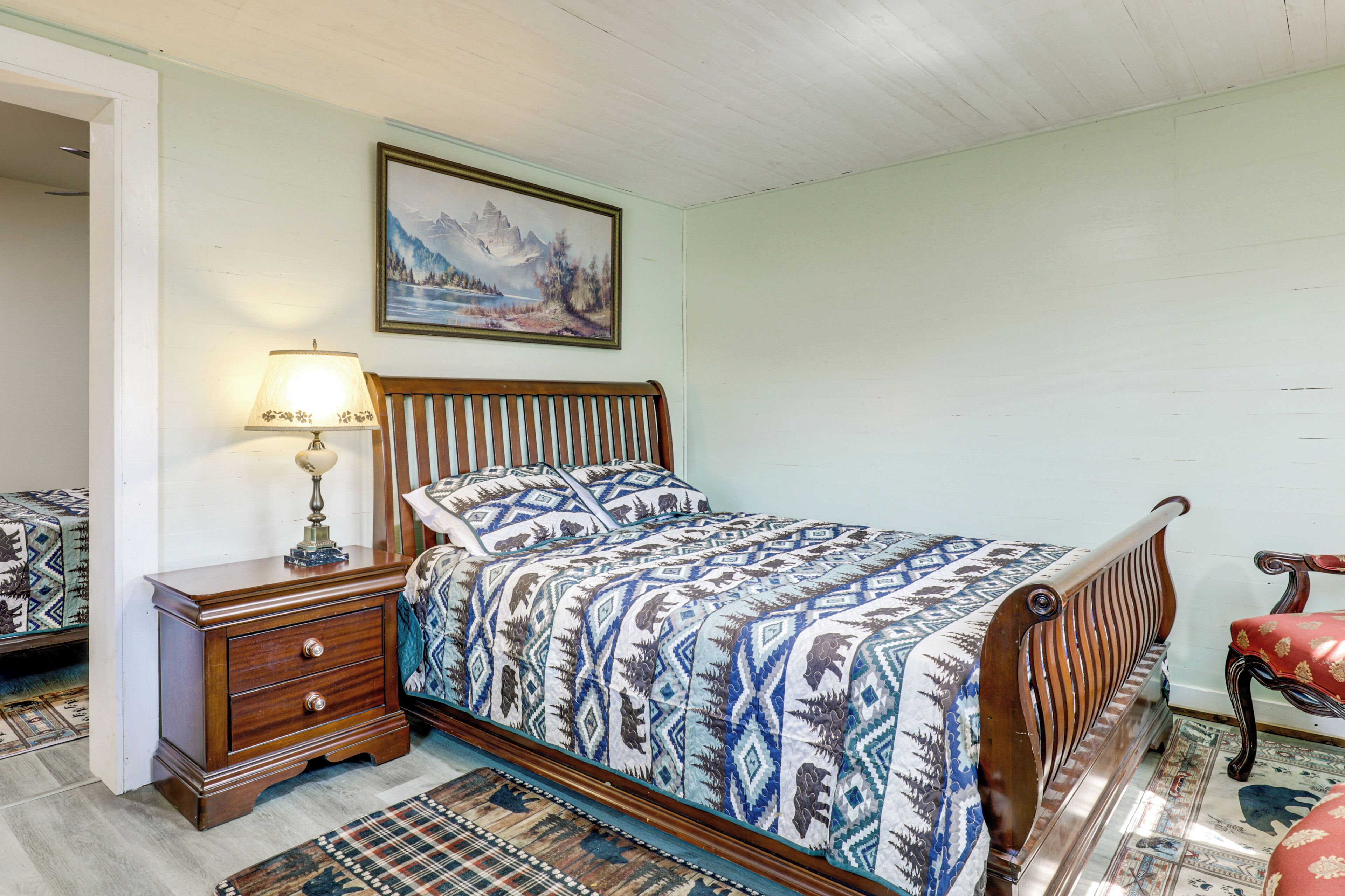 Een slaapkamer met een bed, nachtkastje, lamp, stoel en een schilderij aan de muur.