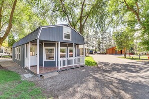 Eine kleine, zweistöckige Holzhütte mit Veranda, umgeben von Bäumen.