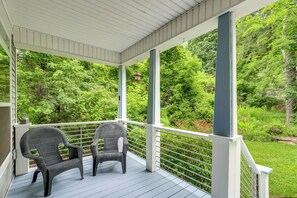 Eine überdachte Veranda mit zwei Korbstühlen, weißen Geländern und Blick auf üppiges Grün.