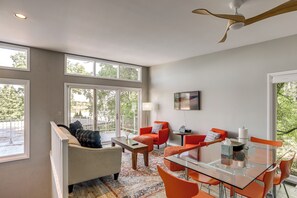 Ein modernes Wohnzimmer mit einem Glastisch, orangefarbenen Sesseln, einem weißen Sofa und großen Fenstern.