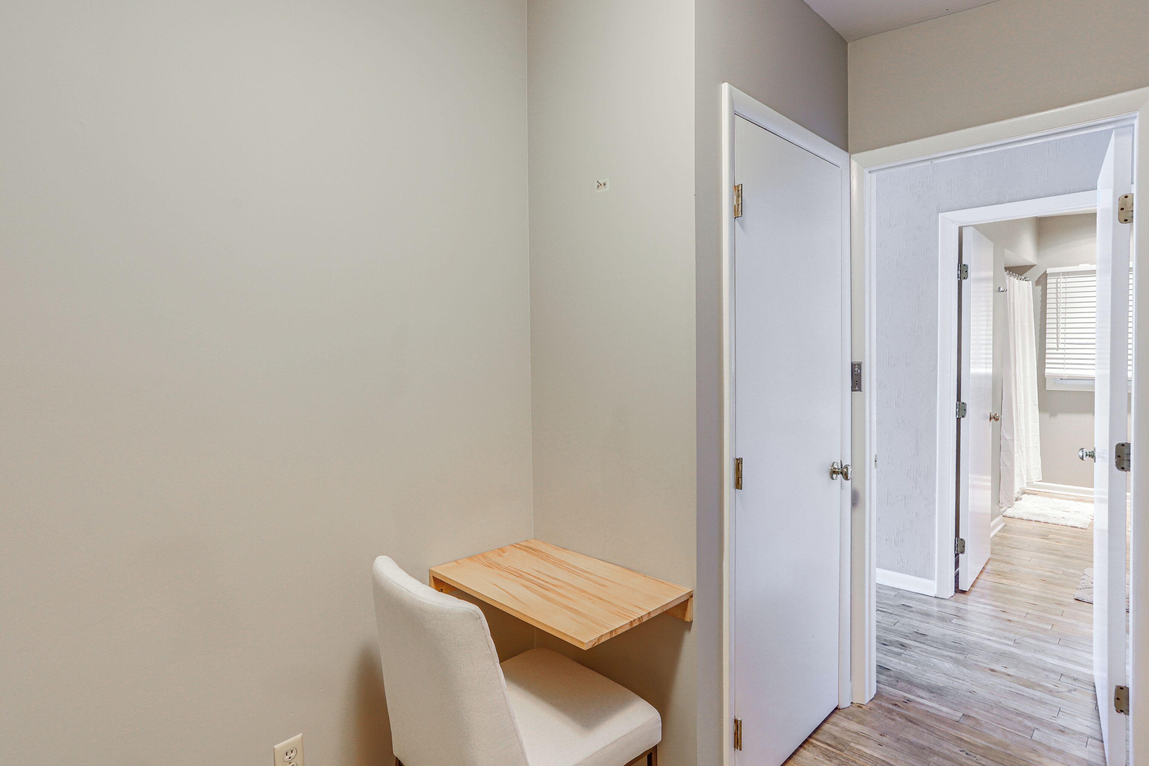 A room with a wooden desk, a white chair, and a door leading to another room.