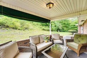 A covered patio area with wicker furniture, a glass table, and a view of a grassy yard. - 7 Mi to Lake Chatuge! Family Home w/ Office & Yard (Hayesville)