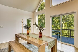 Una habitación con un banco de madera, dos jarrones con plantas, una ventana con vistas a una terraza, y una puerta.