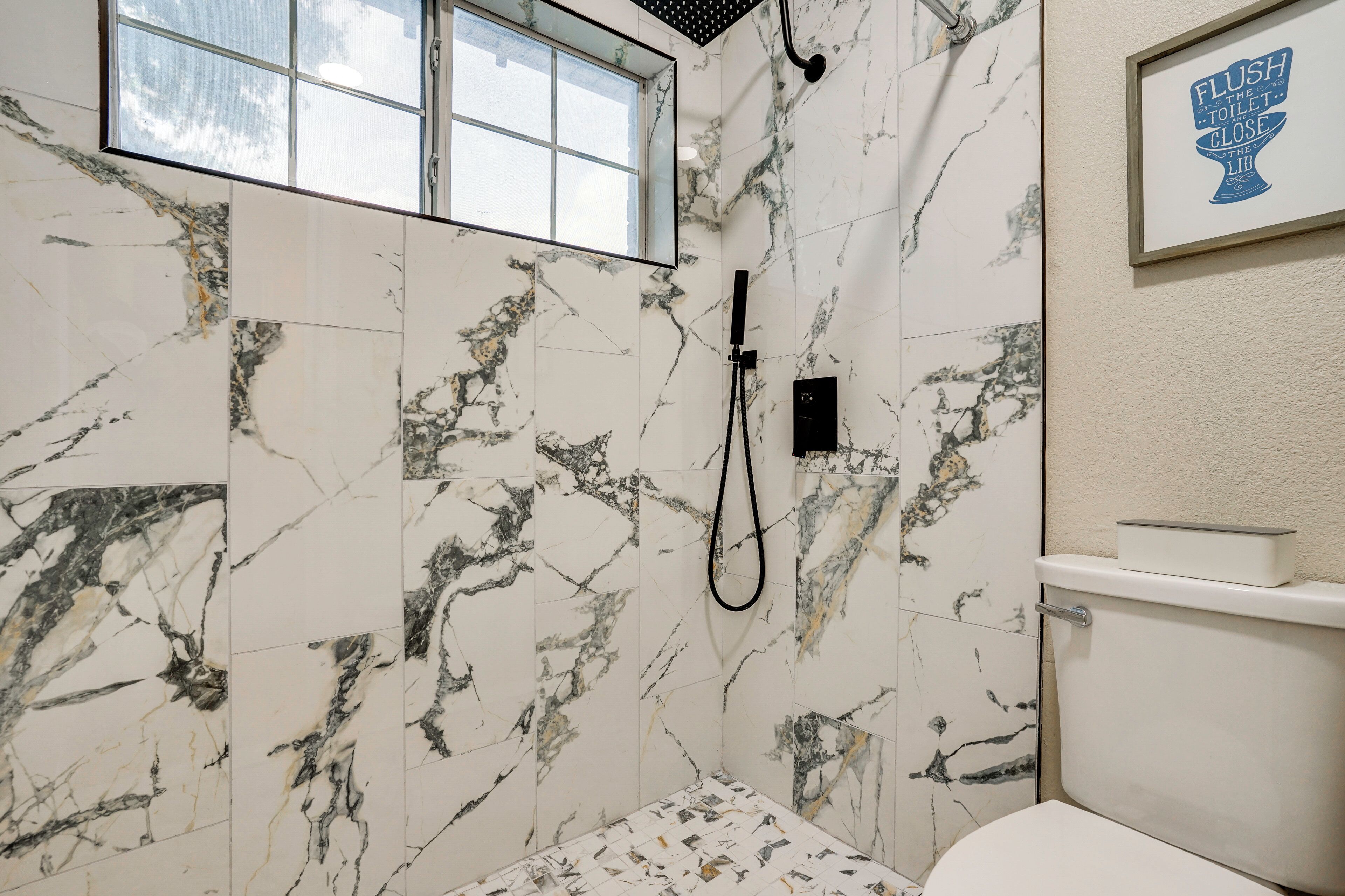 Un baño con paredes de mármol, ducha, inodoro y ventana.