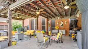 Eine Terrasse im Freien mit Backsteinmauer, gelben Stühlen, einem Tisch, Deckenventilatoren und einem Solarmodul.