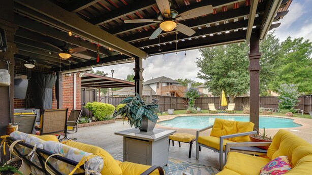 Eine Terrasse im Freien mit gelben Stühlen, einem Pool und einem Deckenventilator.