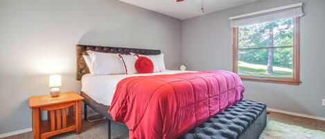 A bedroom with a bed, a nightstand, a bench, a ceiling fan, and a window.