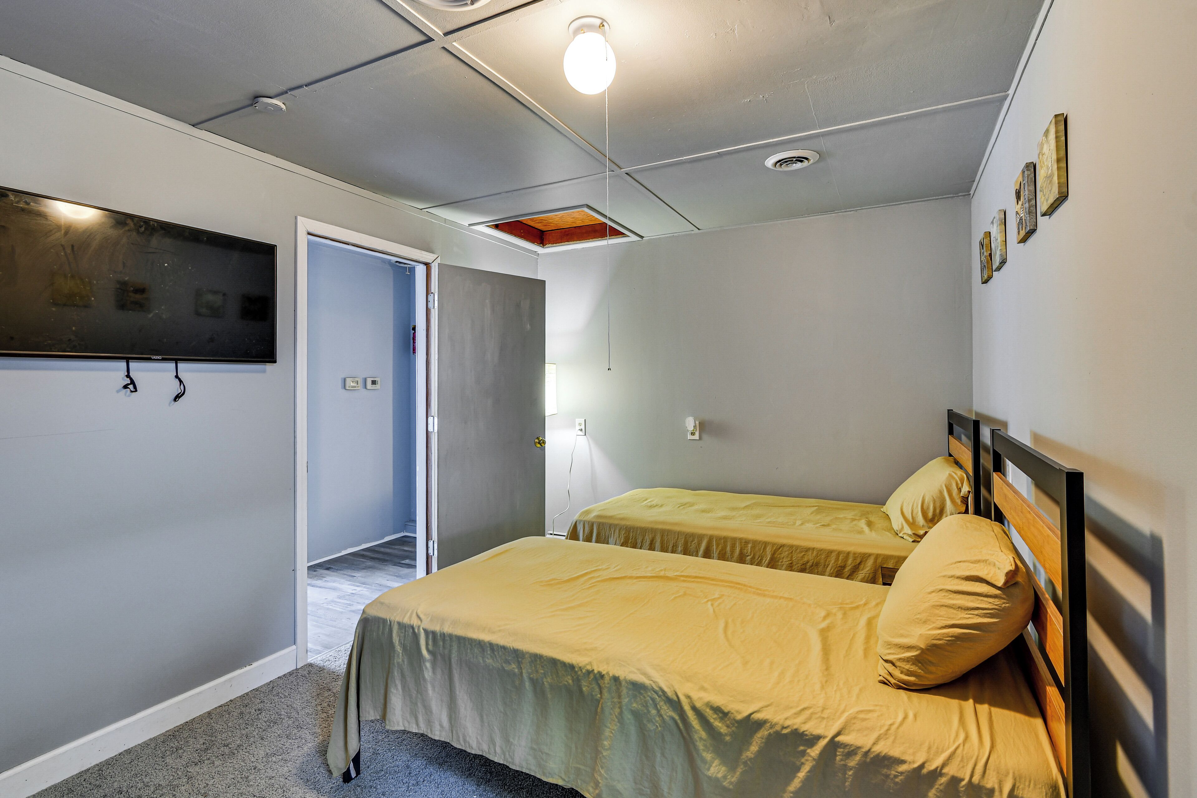 A room with two beds, a ceiling light, a TV, and a door leading to another room.