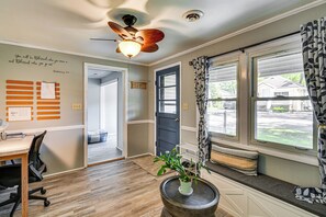 A room with a ceiling fan, a desk with a chair, a window with patterned curtains, and a door. - Shop, Dine, Walk to Houghton Lake! Family Getaway (Prudenville)