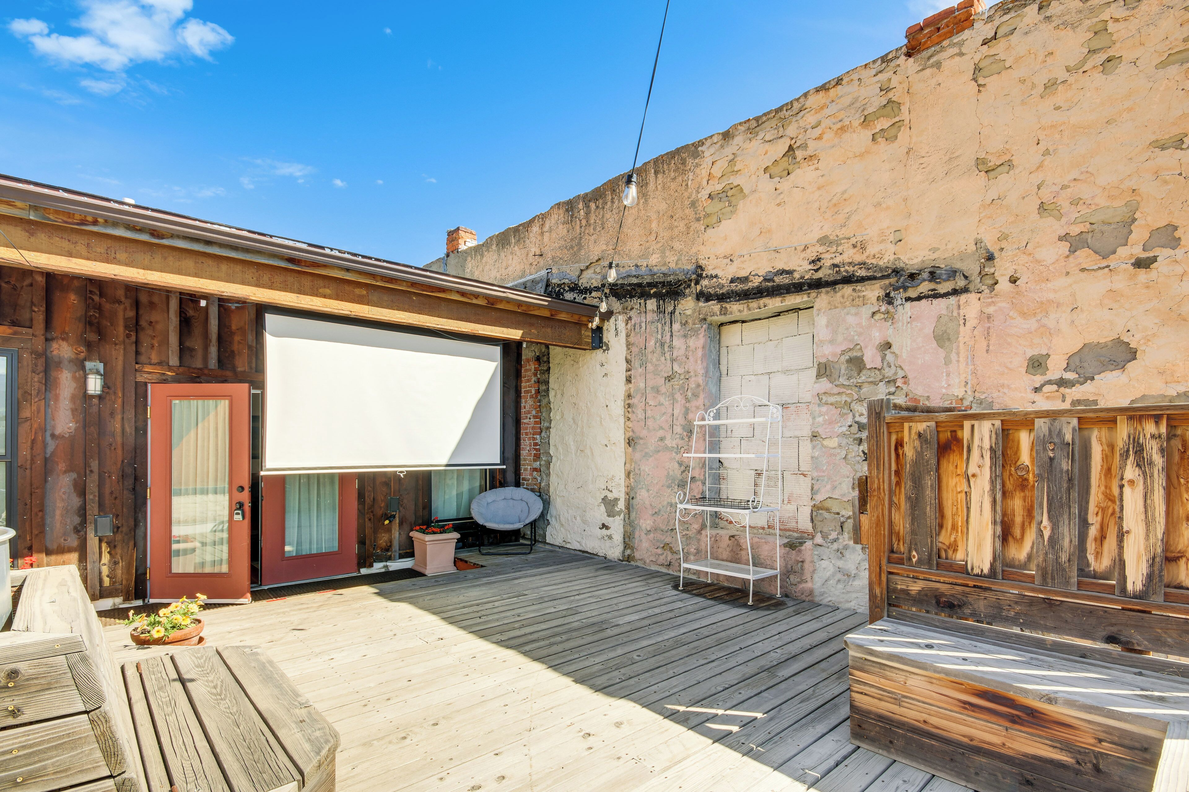 A wooden deck with a white screen, a metal bench, and a red door.