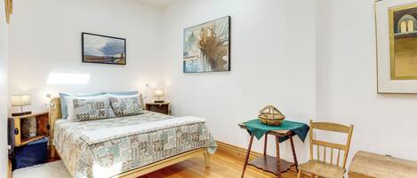 A bedroom with a bed, bedside tables, a chair, a table with a basket, and artwork on the walls.