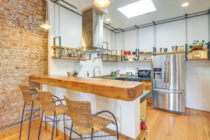 A kitchen with a wooden bar, wicker chairs, a stainless steel refrigerator, and a brick wall. - Stroll to Main St: Livingston Gem w/ Rooftop Deck (Livingston)
