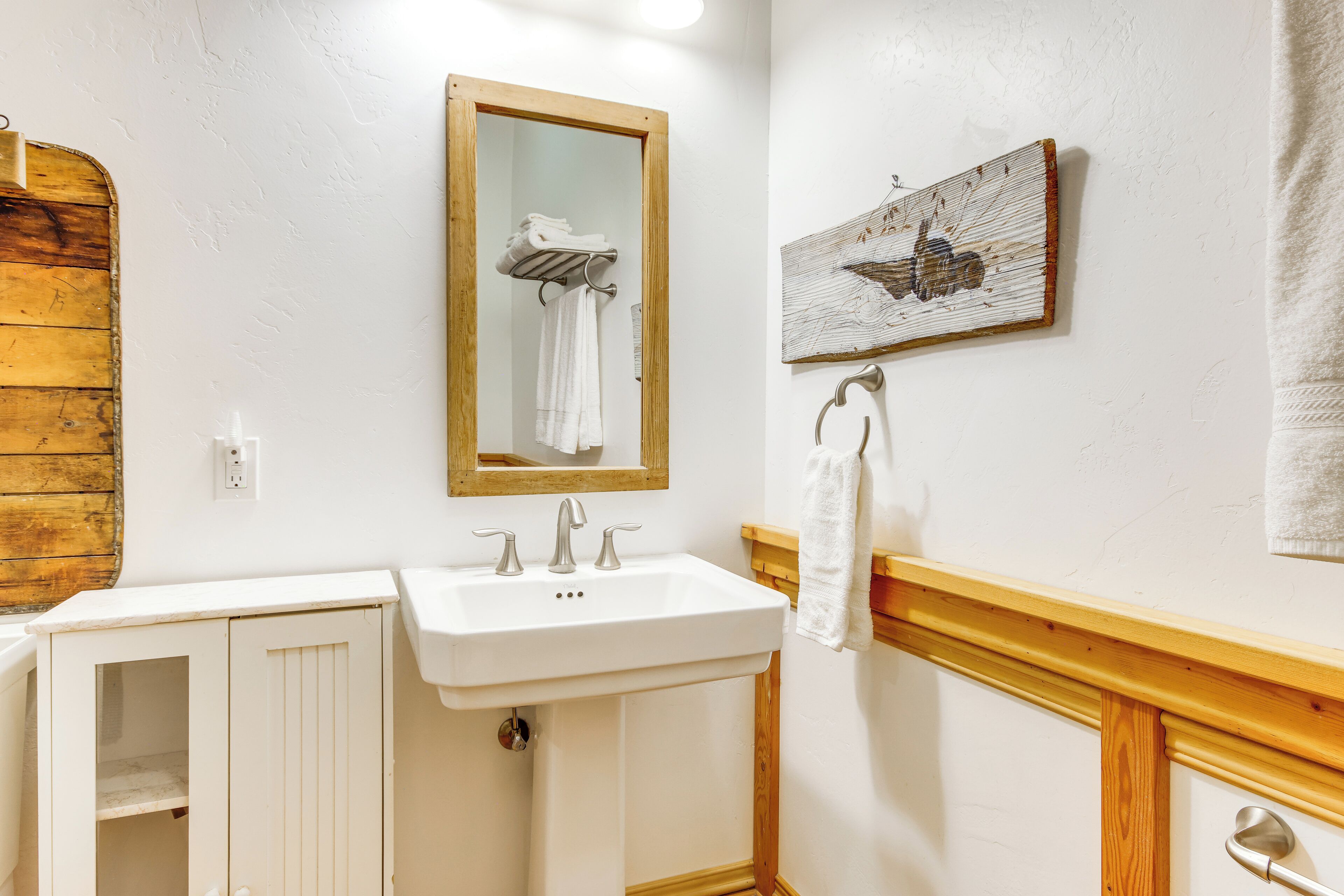 A bathroom with a wooden vanity, a sink, a mirror, and a towel rack.