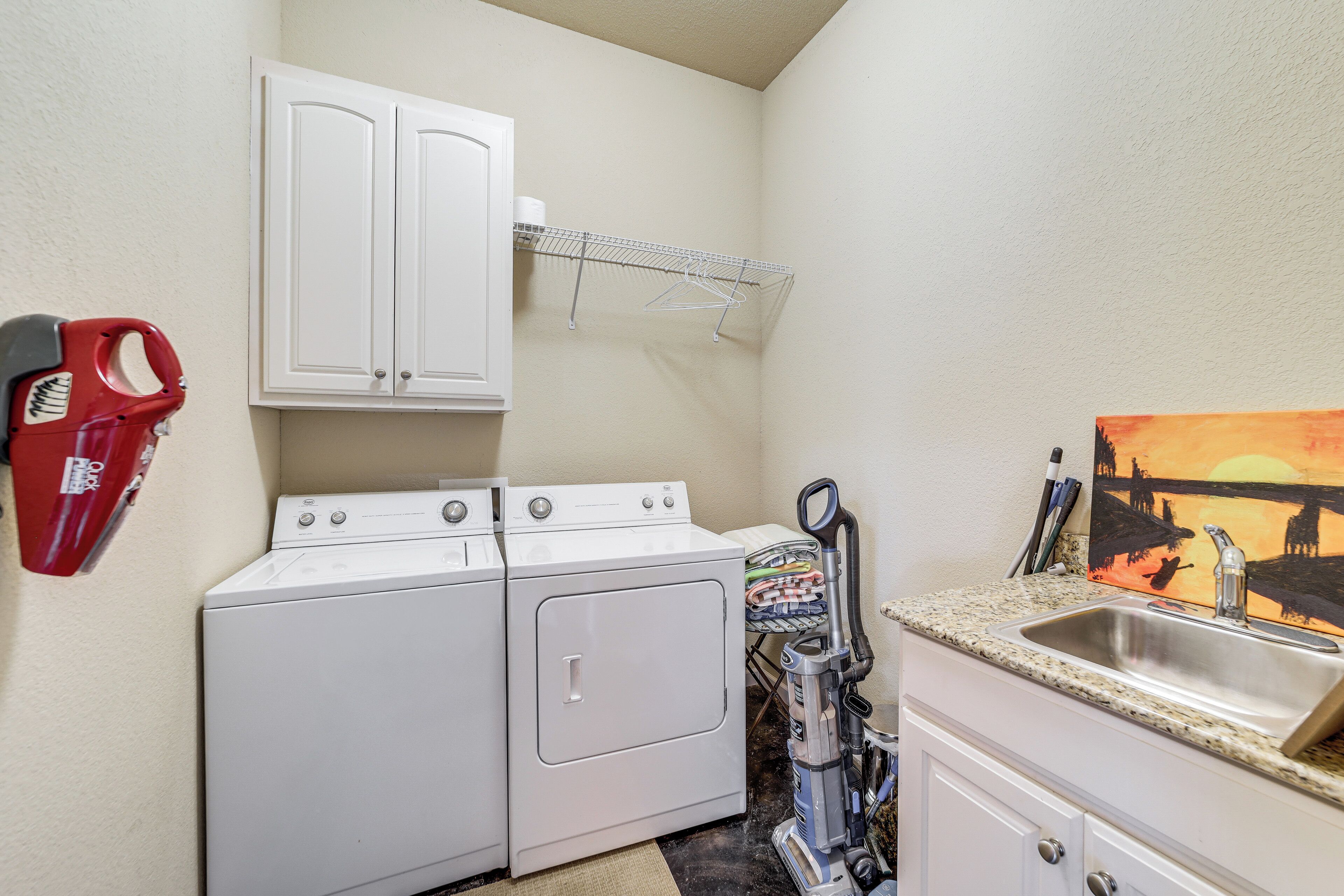 A laundry area with a washer and dryer, a sink, and a painting on the wall.