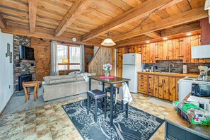 A rustic cabin interior with a fireplace, wooden dining table, sofa, and kitchen area. - Woodland Views: Romantic Hudson Valley Hideaway (Earlton)