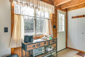 A cabin interior with a wooden interior, a kitchenette with a toaster, a window with curtains, and a door with a coat rack. - Woodland Views: Romantic Hudson Valley Hideaway (Earlton)