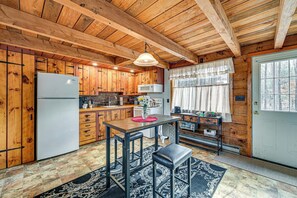 A wooden cabin interior with a kitchen, dining area, and a door. - Woodland Views: Romantic Hudson Valley Hideaway (Earlton)