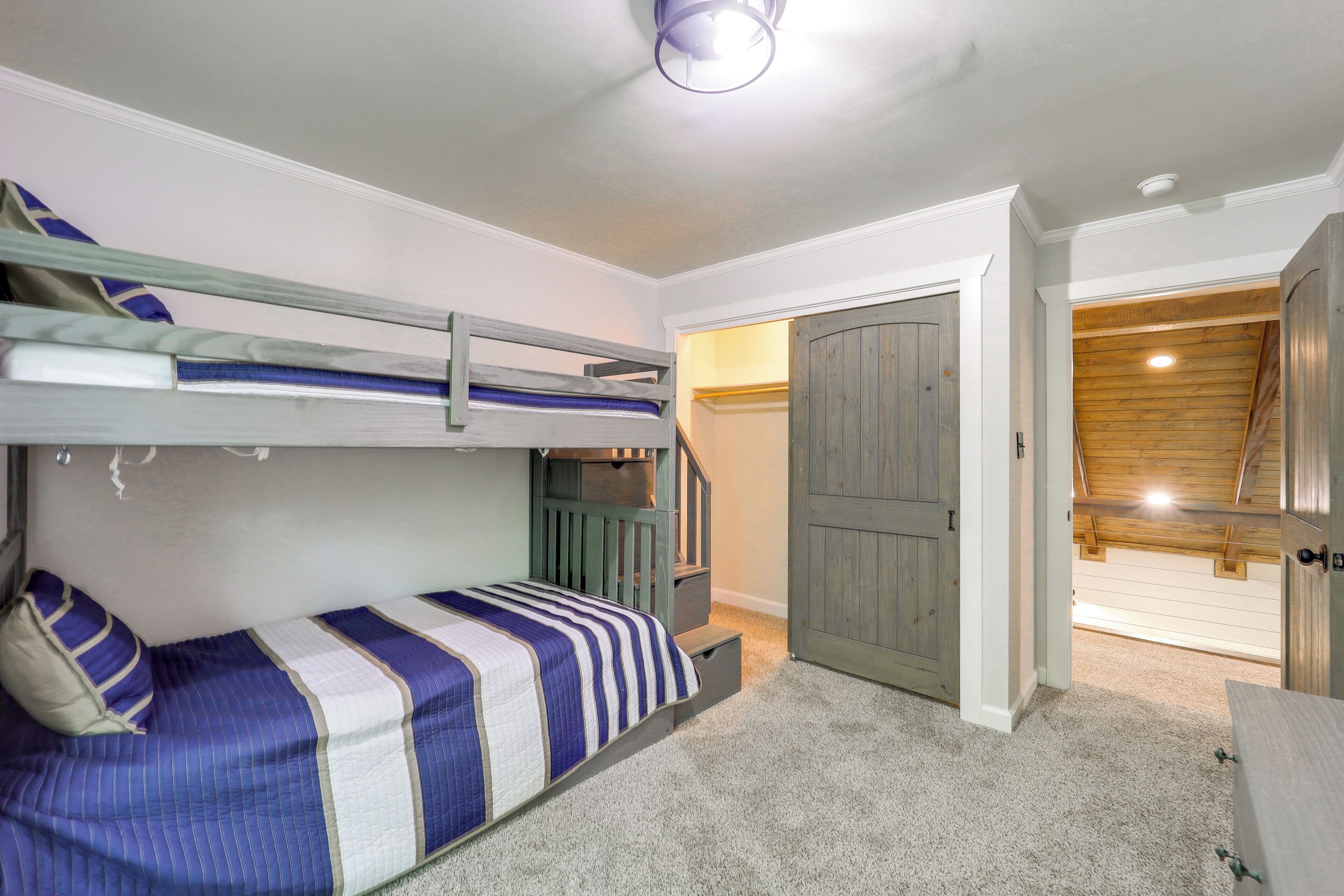 Un dormitorio con literas, una escalera y una puerta que da a otra habitación.