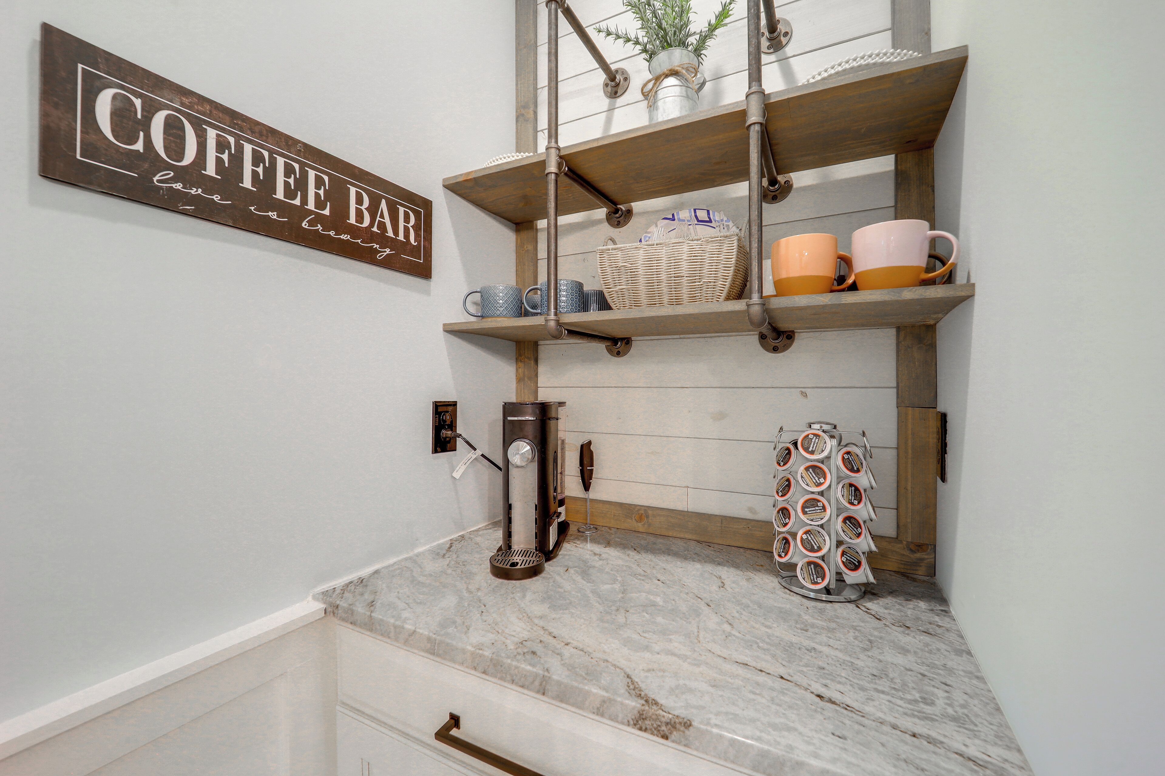 Una cocina con barra de café, estantes con tazas, una cafetera y un cortador de queso.