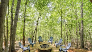 A circular stone fire pit surrounded by six Adirondack chairs in a forest setting. - Resort Perks & Game Room! Group Escape in Deep Gap (Deep Gap)