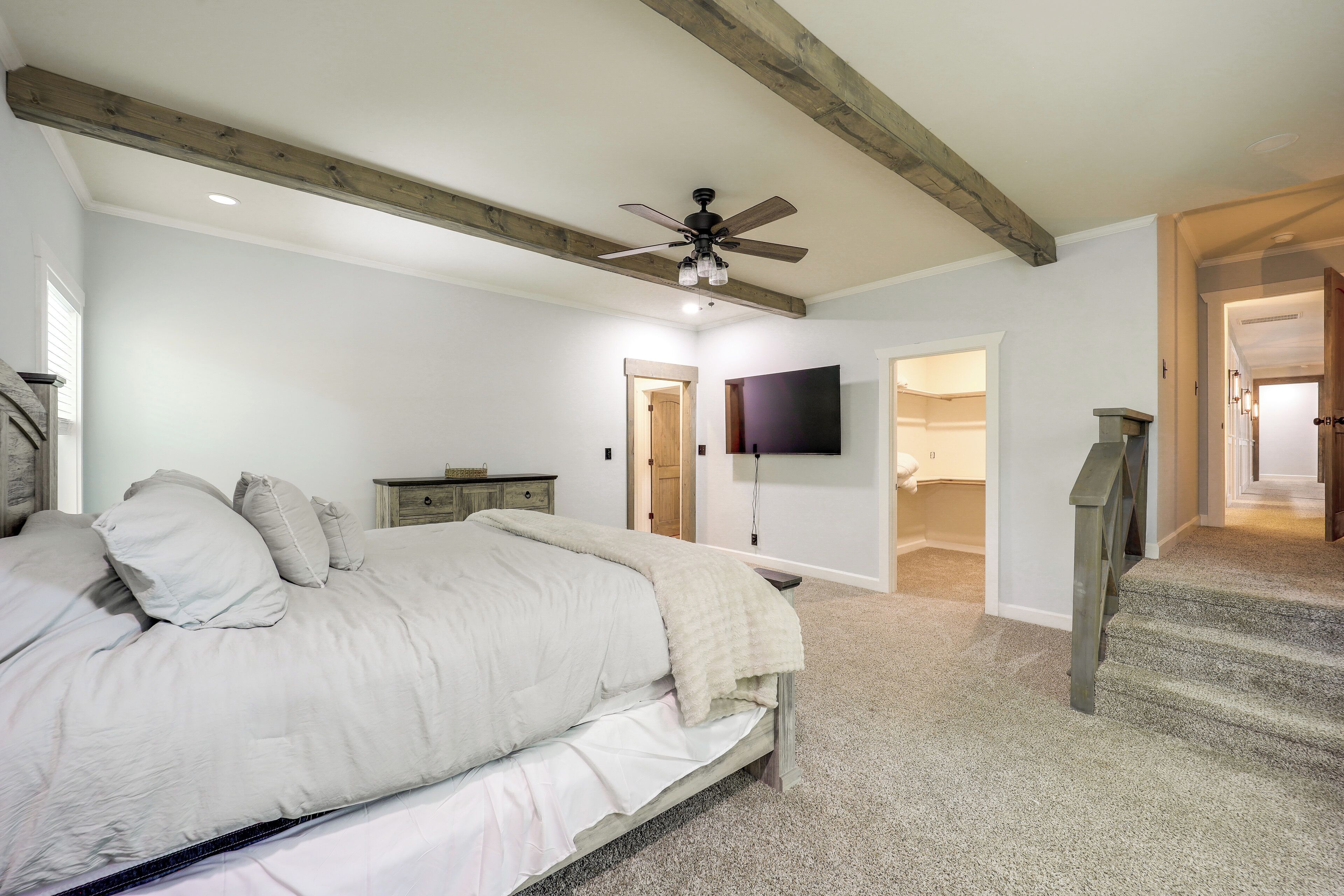 A bedroom with a bed, a ceiling fan, a TV, and a staircase.