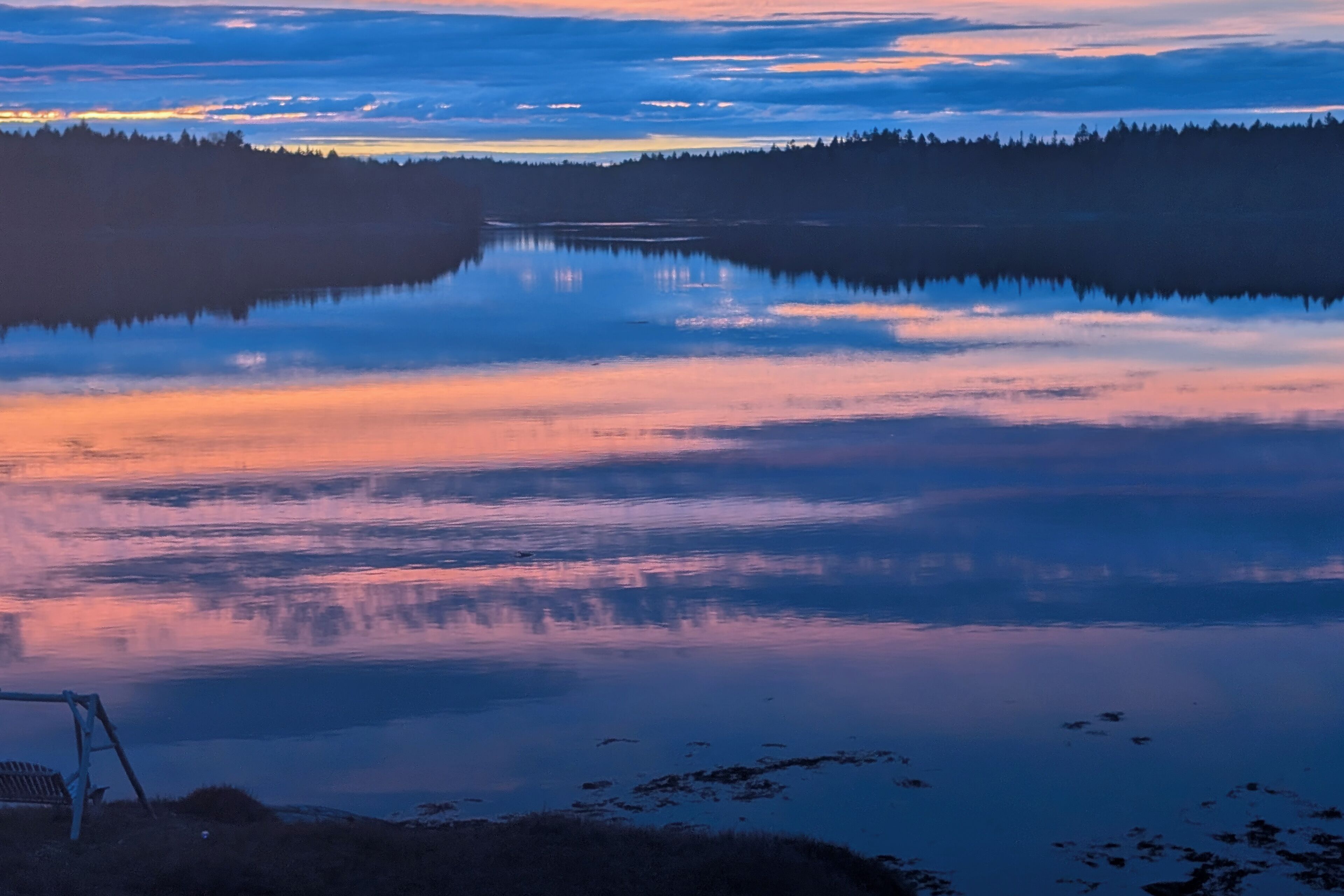 A serene lakeside view with a bench and calm water reflecting the sky.