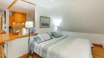 A bedroom with a bed, bedside table, lamp, and a view of the kitchen.