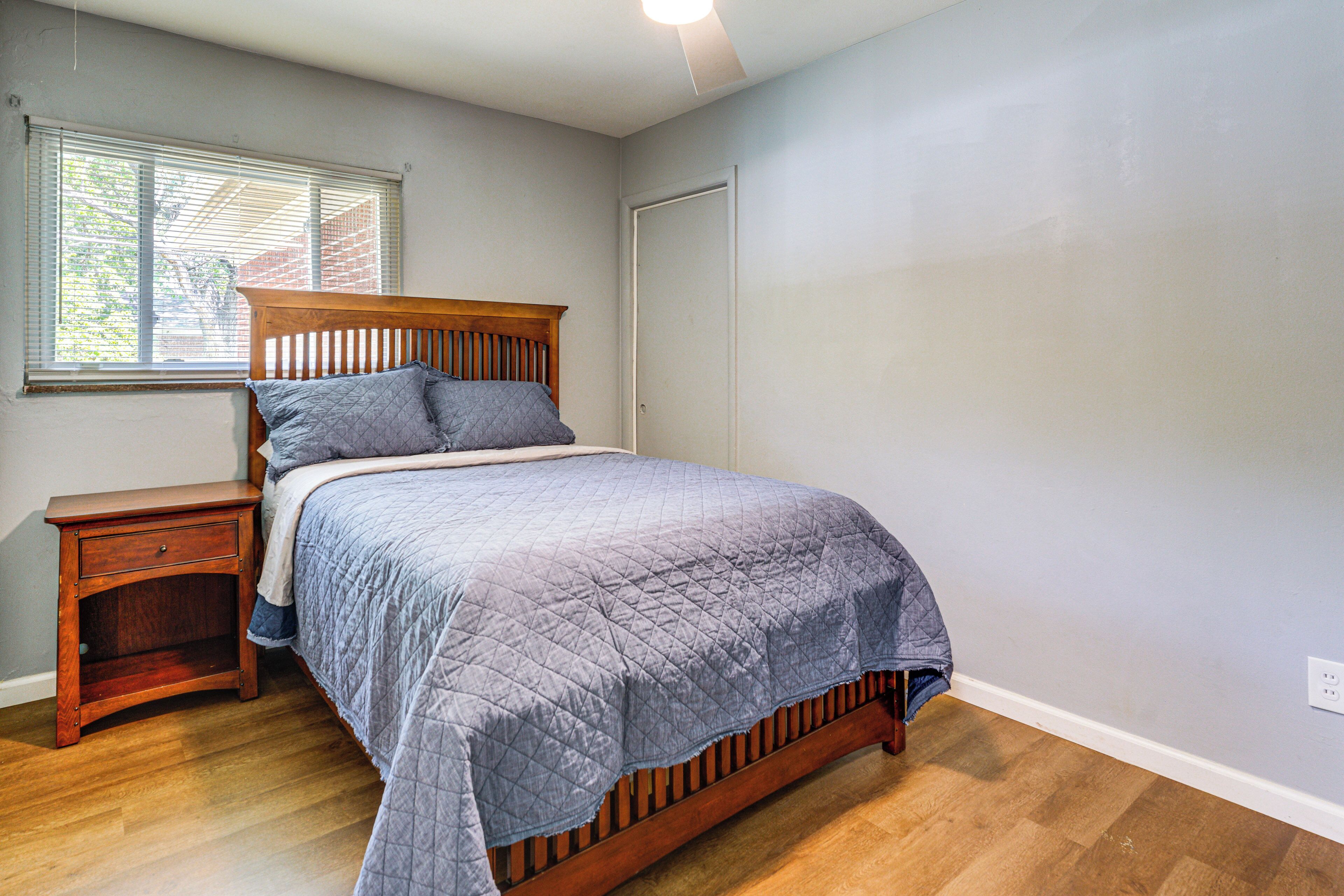A bedroom with a wooden bed, a nightstand, a window with blinds, and a door.