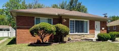 A single-story brick house with a front porch, a small front yard, and a clear blue sky.