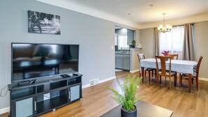 Una sala de estar moderna con un televisor de pantalla plana, un comedor con mesa y sillas, y una cocina al fondo.