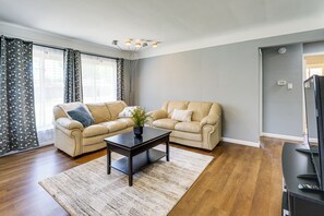 Una sala de estar con dos sofás color beige, una mesa de centro de madera oscura y un ventanal con cortinas traslúcidas.