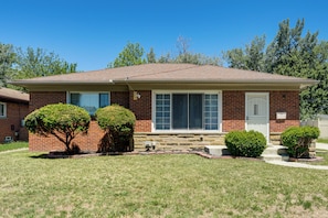 A single-story brick house with a front porch, two small trees, and a clear blue sky. - 4 Mi to Detroit Zoo! Group Retreat w/ Private Yard (Oak Park)