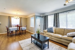A living room with a dining table, chairs, a sofa, a coffee table, and a large window with curtains. - 4 Mi to Detroit Zoo! Group Retreat w/ Private Yard (Oak Park)