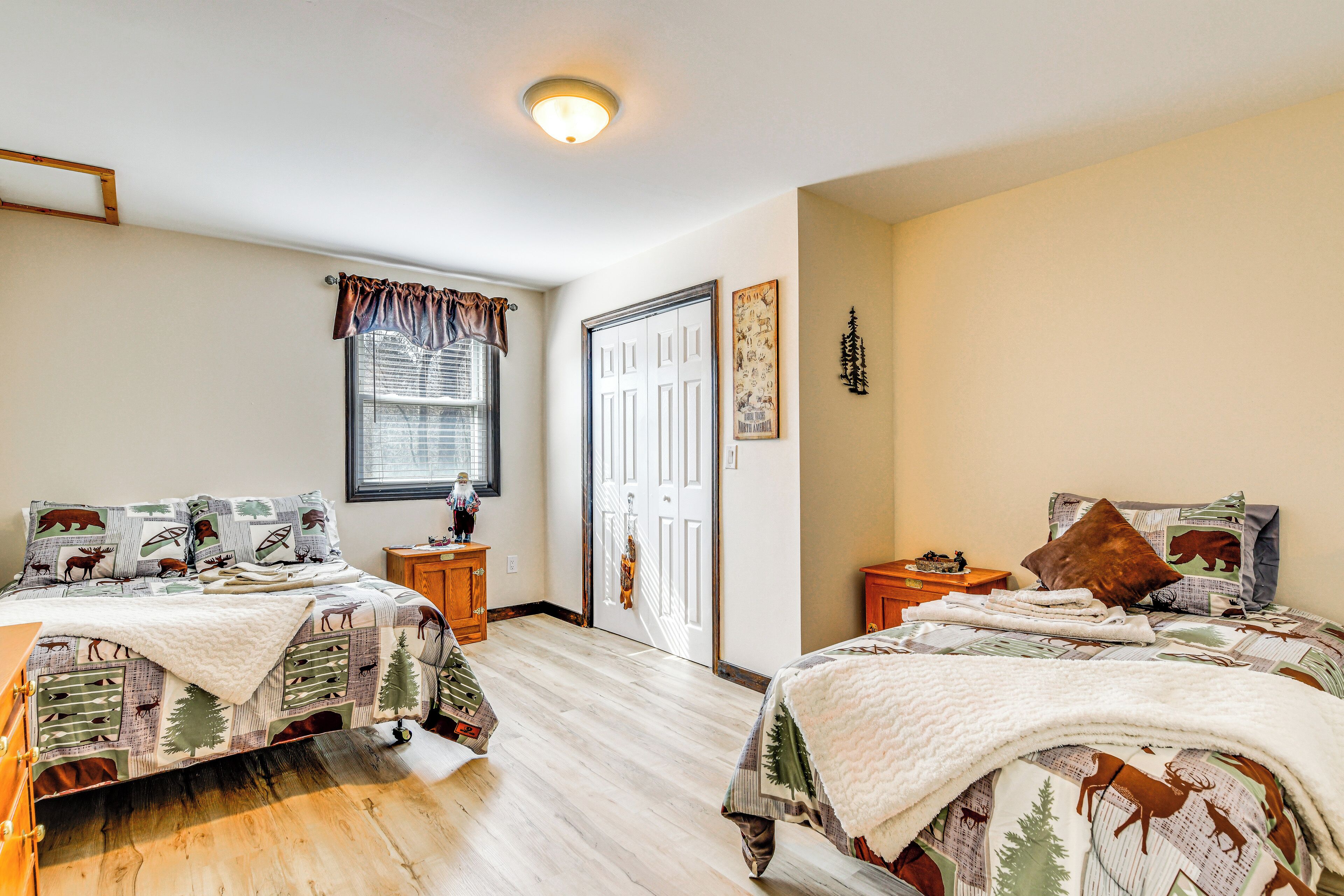 A bedroom with two beds, a window with blinds, a door, and a small wooden nightstand.