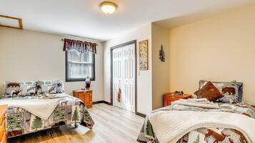 A bedroom with two beds, a window with blinds, a door, and a small wooden nightstand.