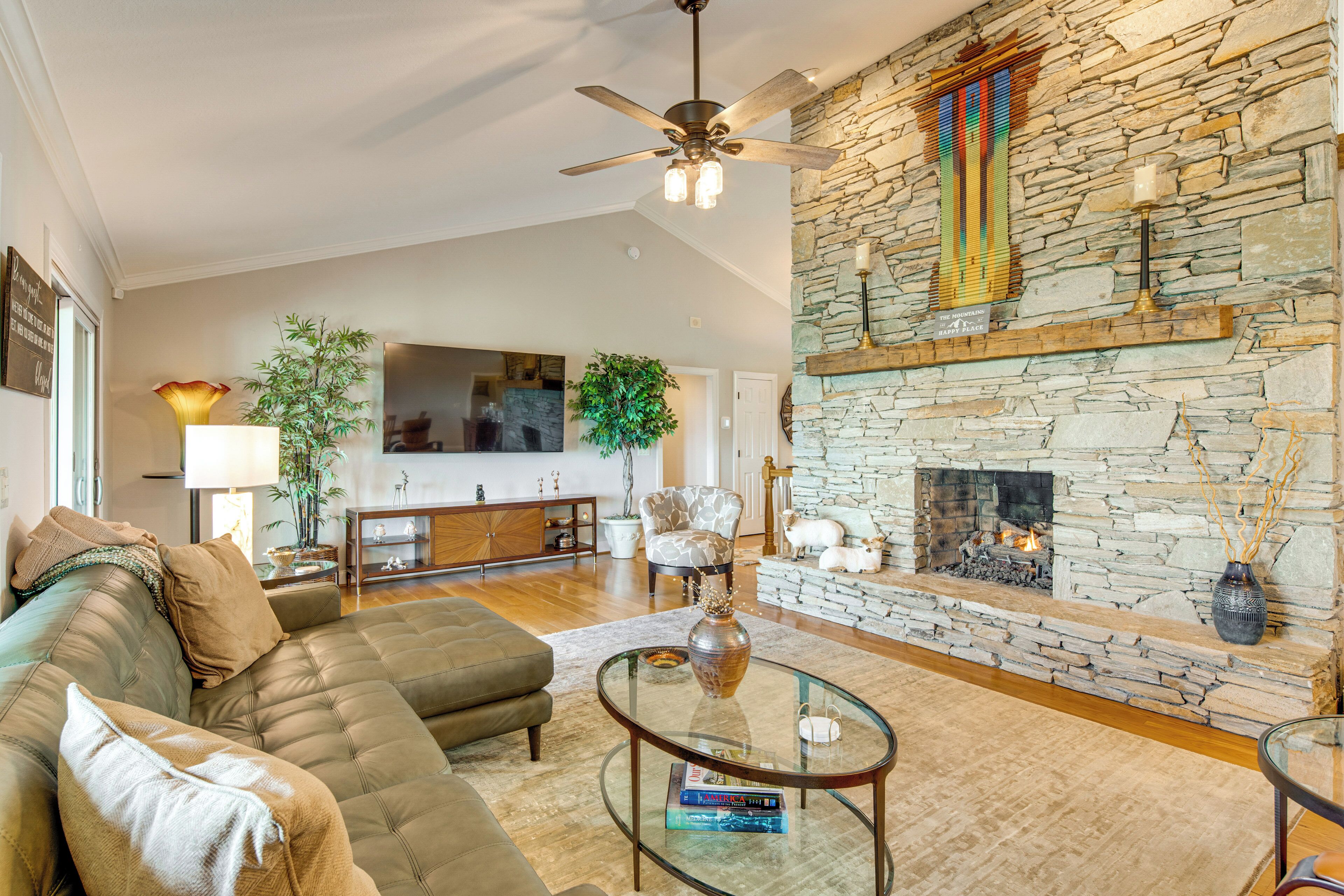 A living room with a stone fireplace, a sofa, a glass coffee table, and a ceiling fan.