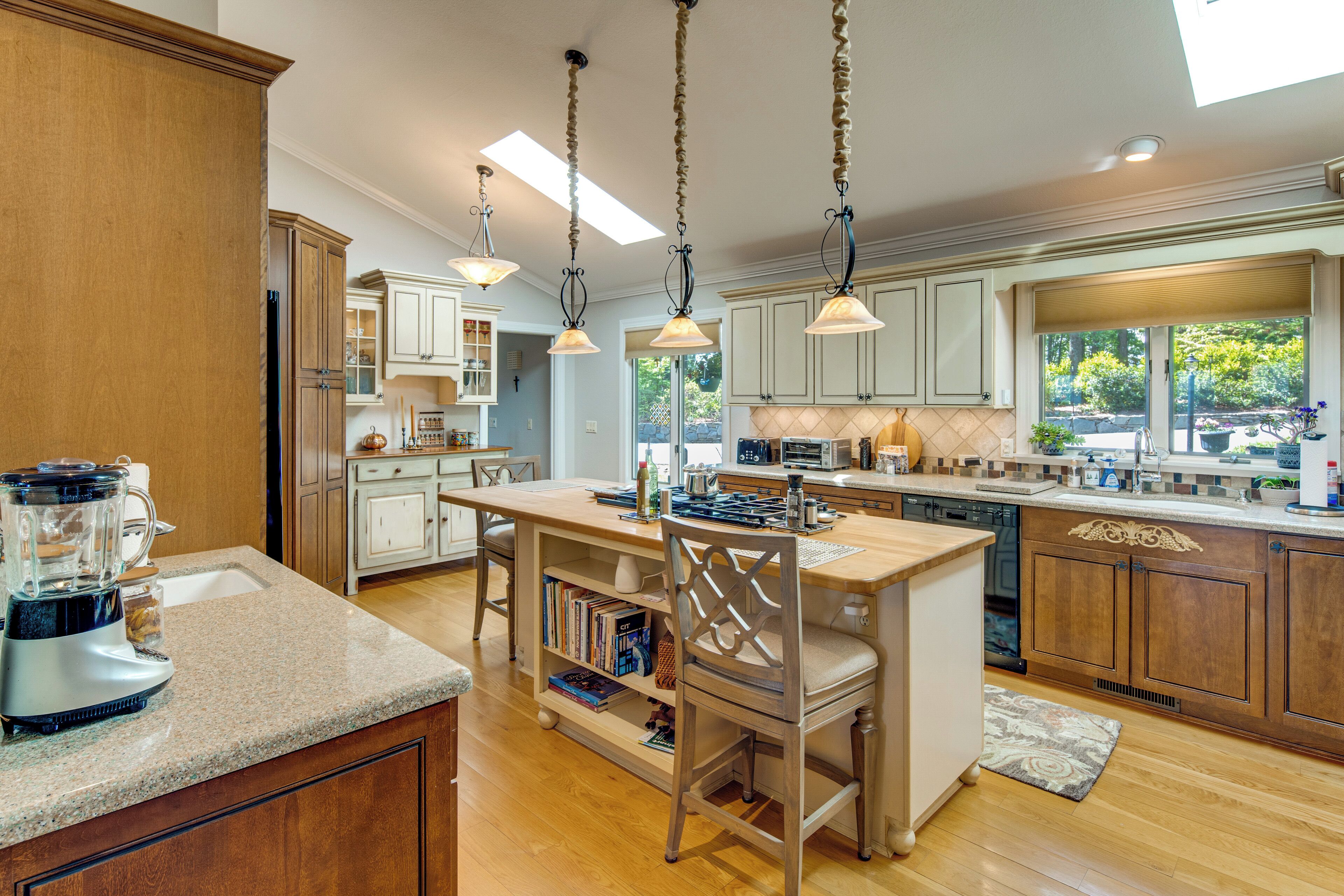 A kitchen with wooden cabinets, a central island, pendant lighting, and a view of the outdoors.