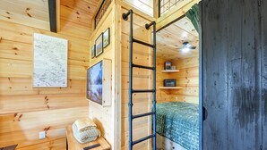 A wooden cabin interior with a ladder, a bed, a shelf with pictures, and a map on the wall.