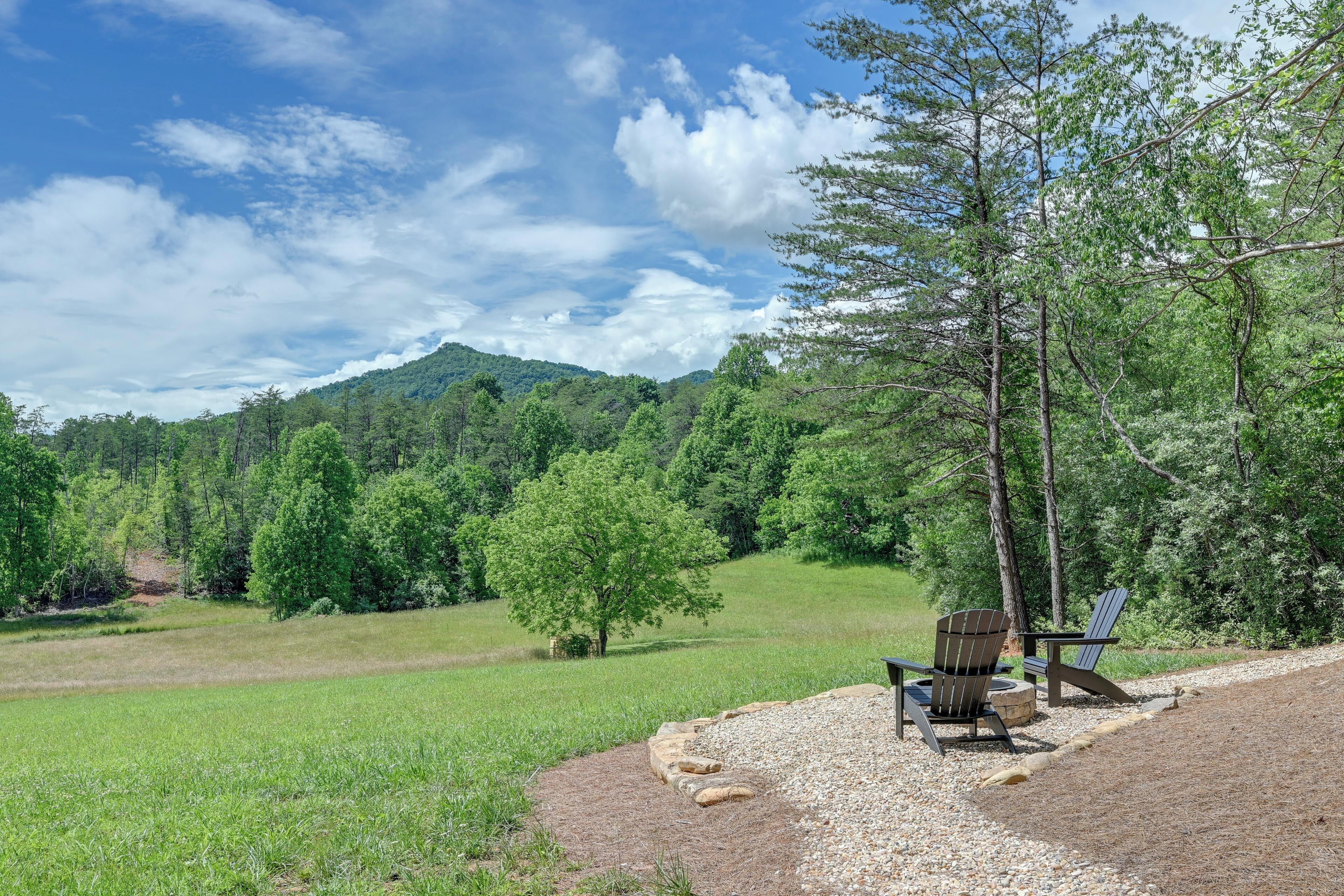 A campsite with a gravel area, two Adirondack chairs, and a view of a forested mountain.