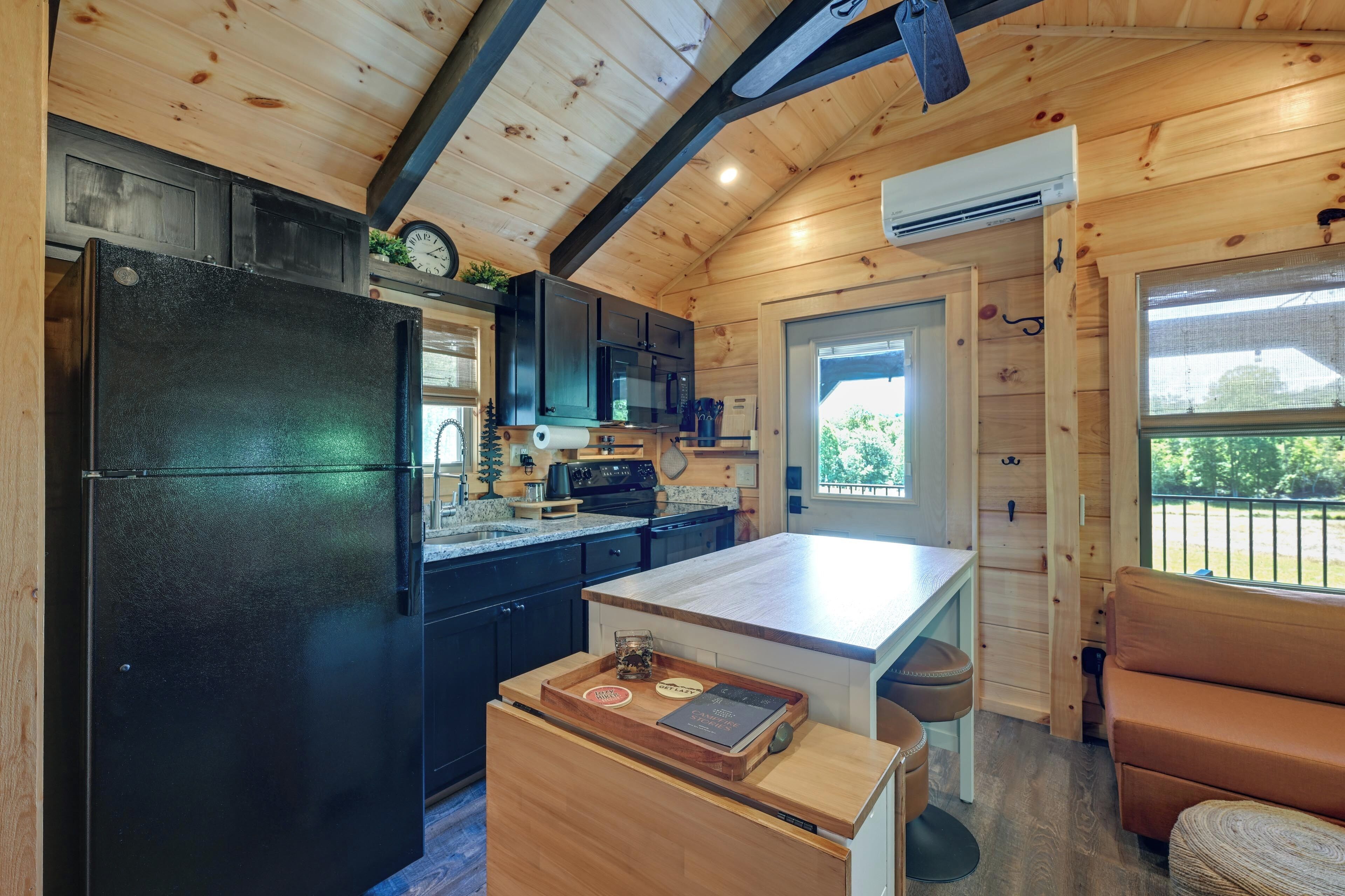 Una cocina compacta con un refrigerador negro, armarios de madera, una encimera y un pequeño comedor con un banco.