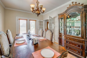 A dining room with a wooden table set for four, chairs, a chandelier, and a large wooden cabinet with glass doors. - Red Oak Group Getaway w/ Yard + Patio (Red Oak)