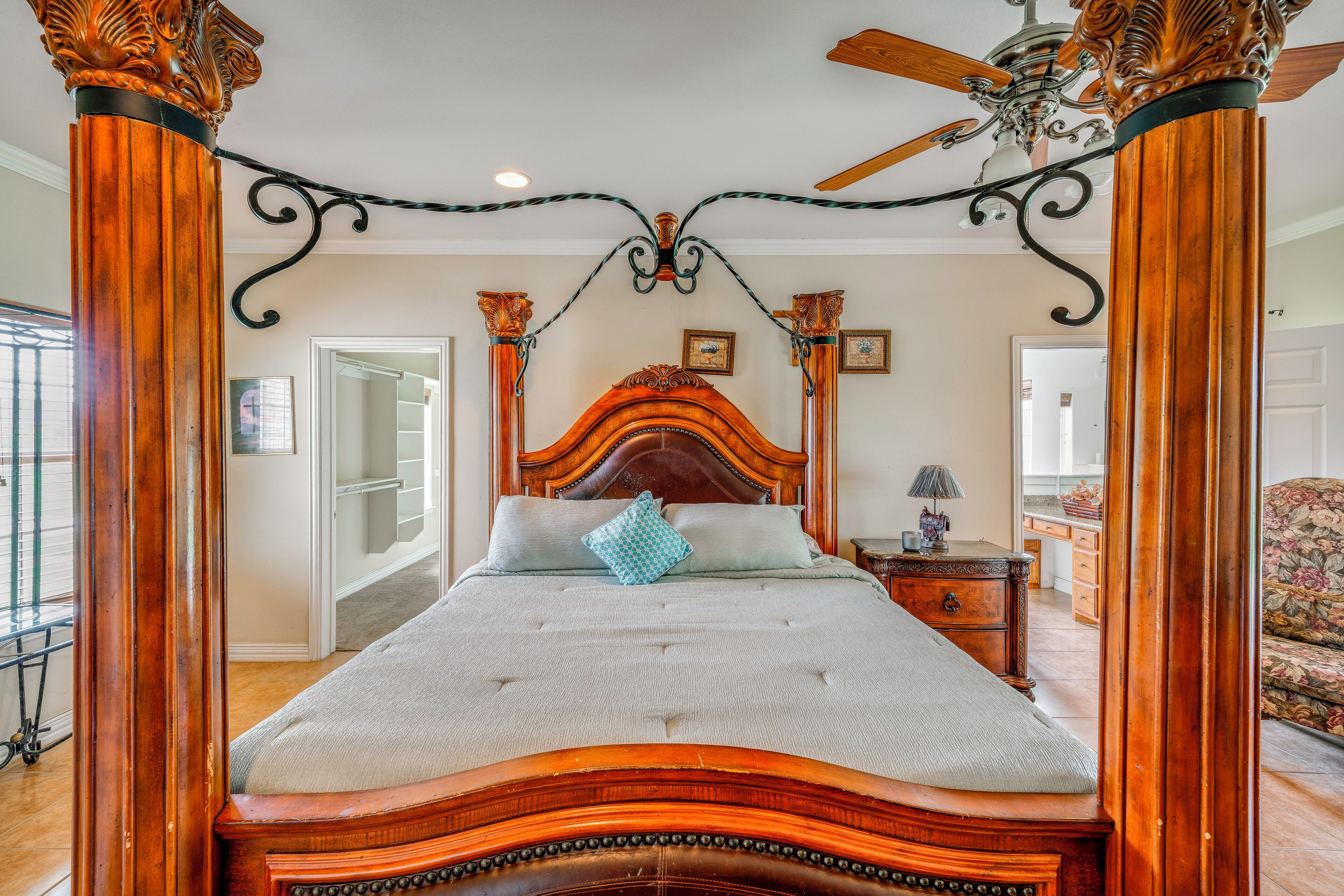 A four-poster bed with a wooden headboard, a ceiling fan, and a view of the adjacent room.