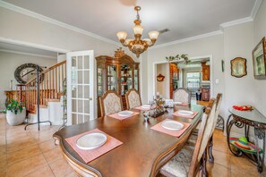 A dining room with a large wooden table set for six, surrounded by chairs, a chandelier, and a mirror.
