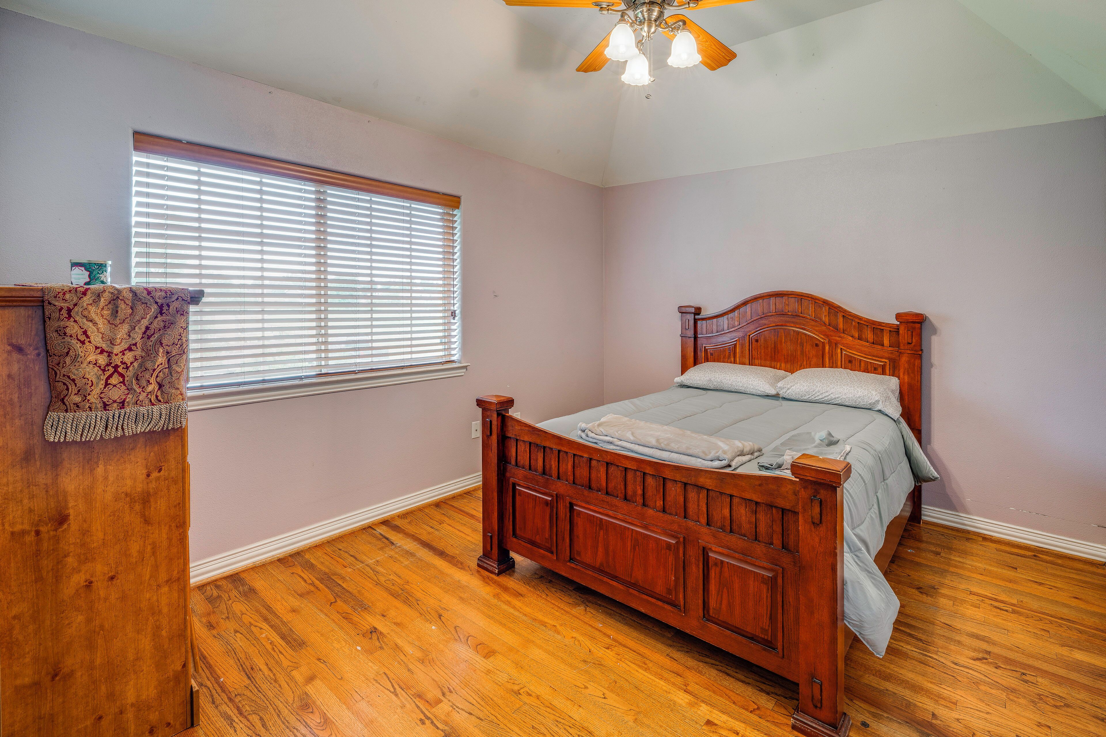A bedroom with a wooden bed, a window with blinds, a ceiling fan, and a wooden dresser.