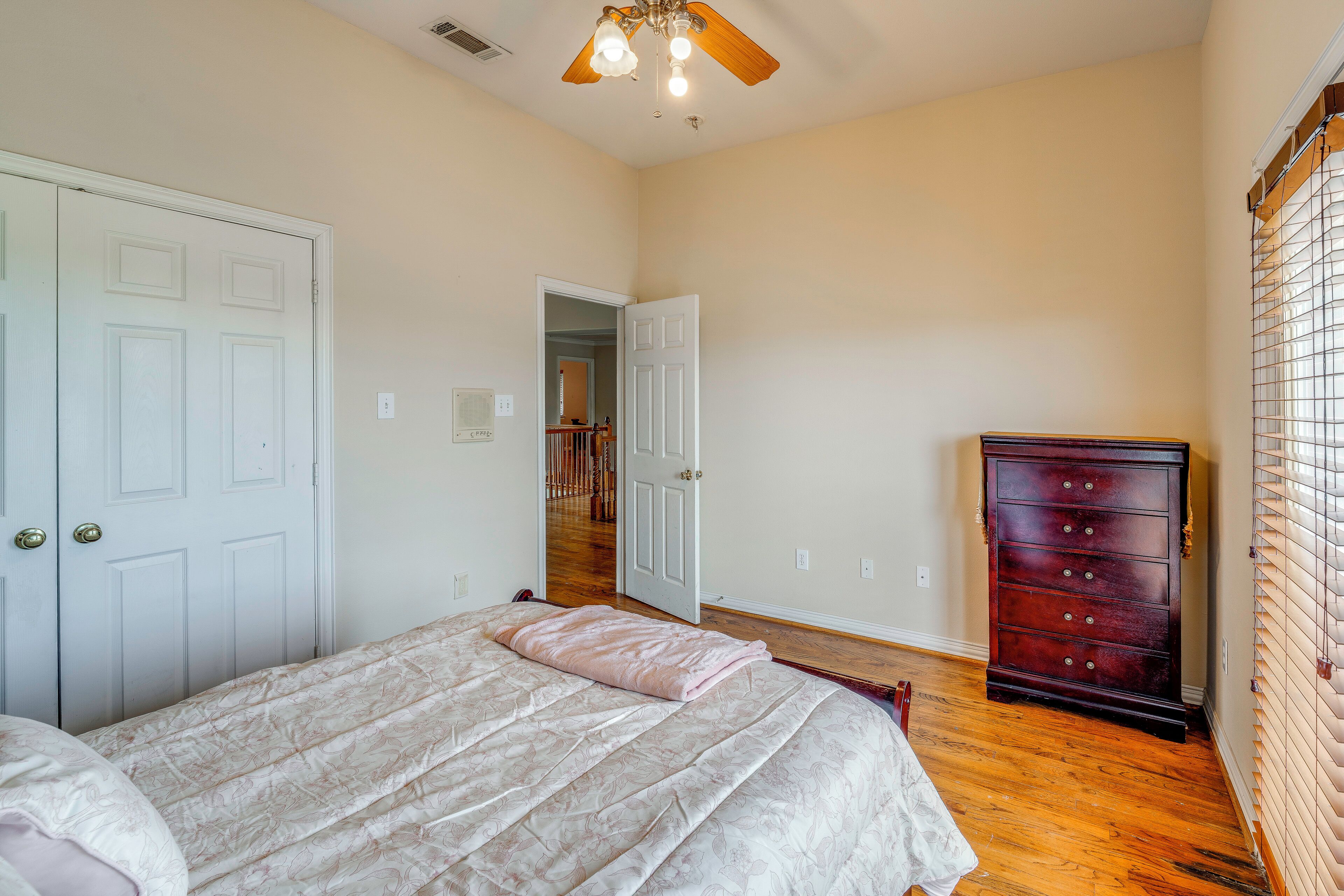 A bedroom with a bed, a dresser, a ceiling fan, and a door leading to a staircase.