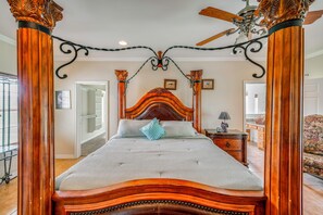 Un lit à baldaquin avec une tête de lit en bois, un ventilateur de plafond et une vue sur la pièce adjacente.